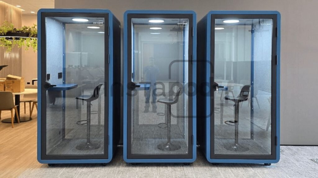 Three glass soundproof booths with chairs inside an office space.