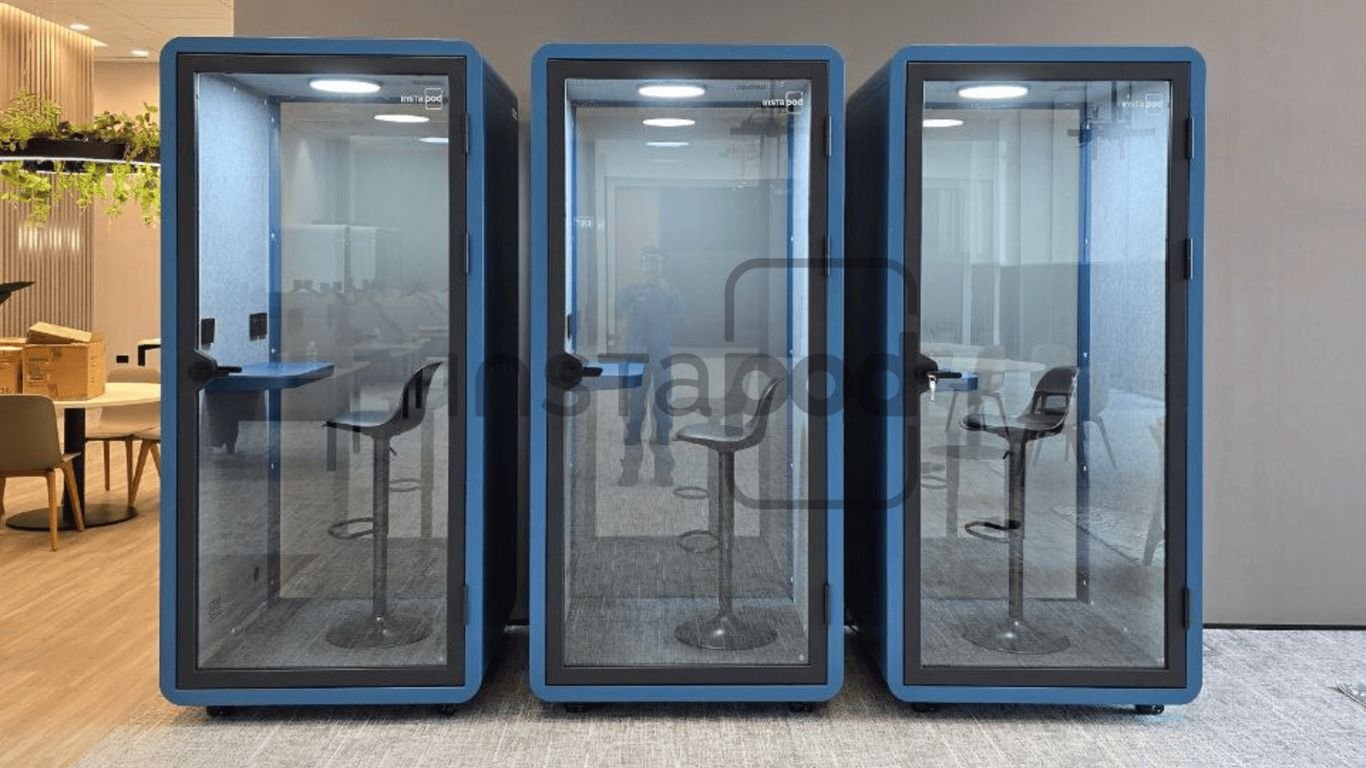 Three glass soundproof booths with chairs inside an office space.