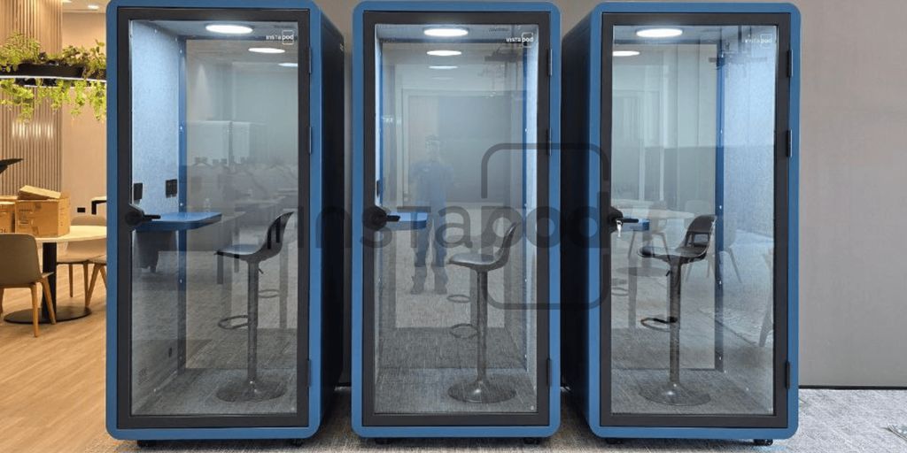 Three glass soundproof booths with chairs inside an office space.
