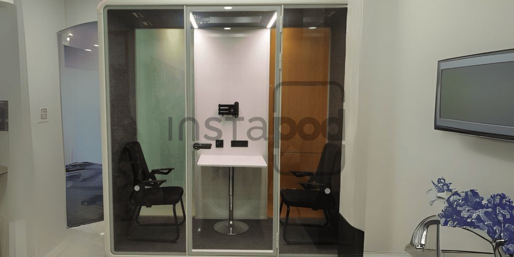 Modern soundproof booth with chairs and a table inside.