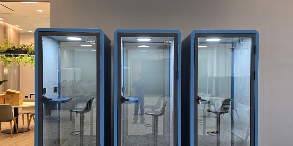 Three glass phone booths in a modern office space.
