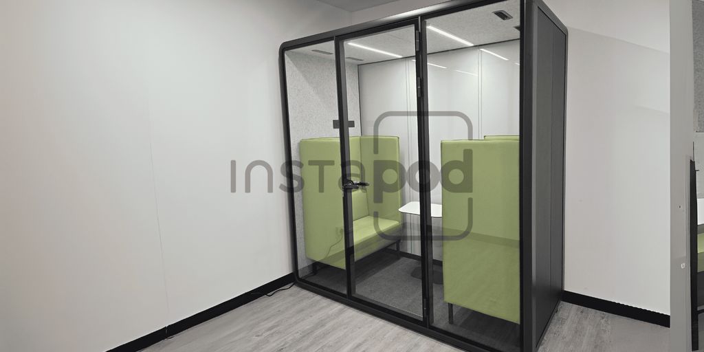 A modern glass pod with green seating for privacy and comfort.