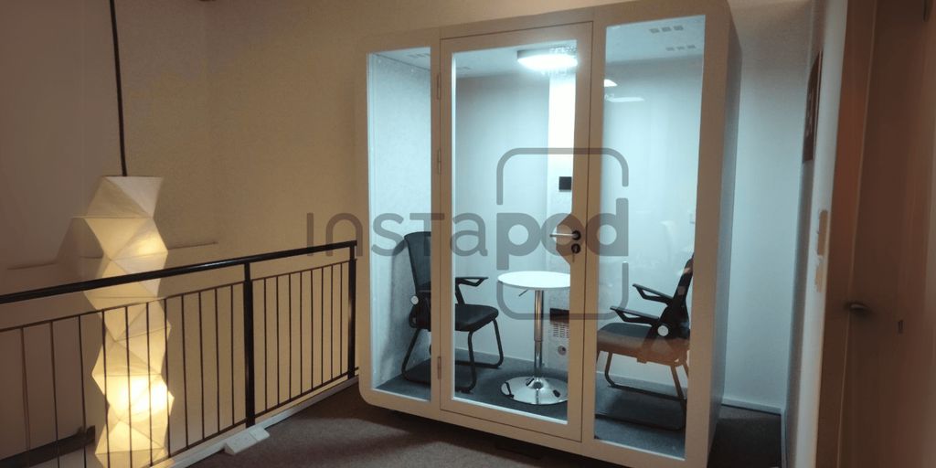 A modern glass meeting pod with two chairs inside.