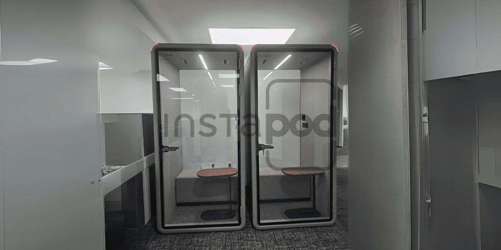 Two modern, glass-walled phone booths in a workspace.