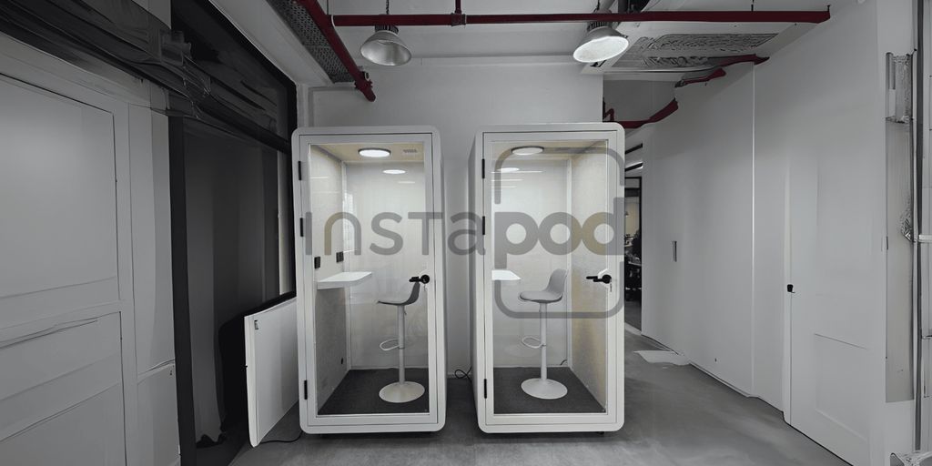Two soundproof booths with chairs in a modern office space.
