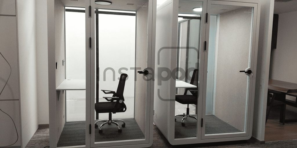Two glass-walled office pods with chairs and desks inside.