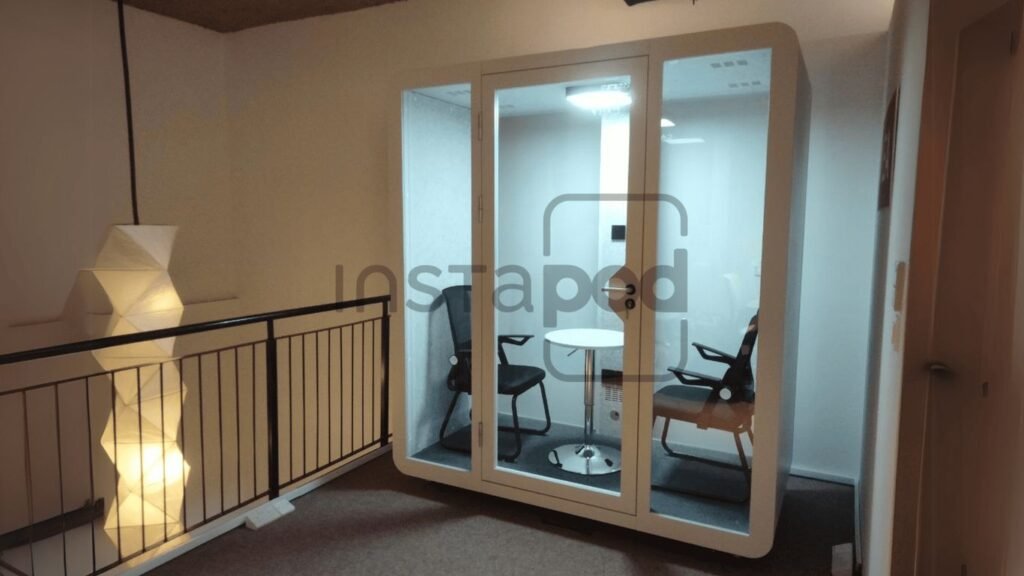 A modern glass meeting pod with two chairs inside.