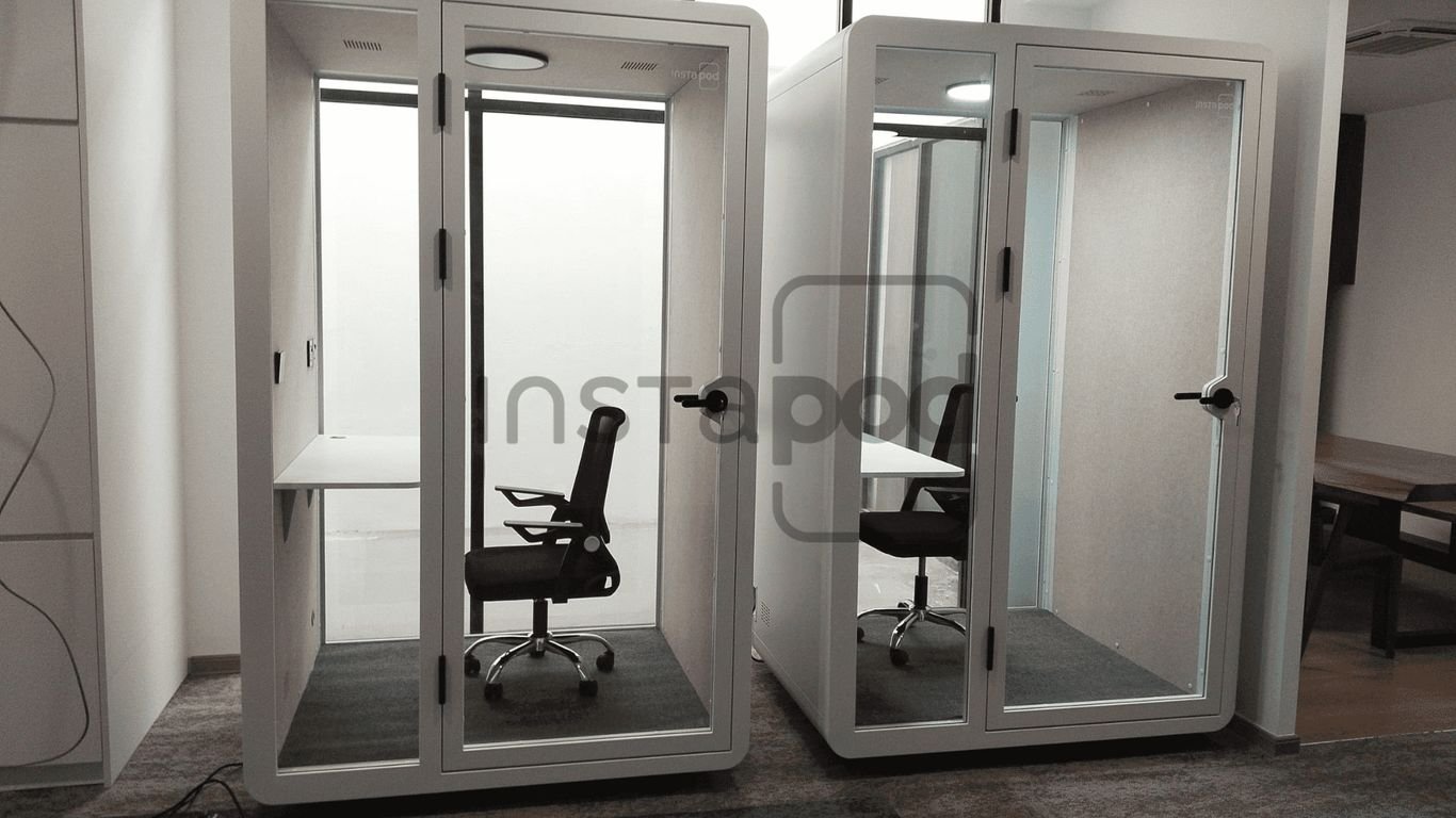 Two glass-walled office pods with chairs and desks inside.