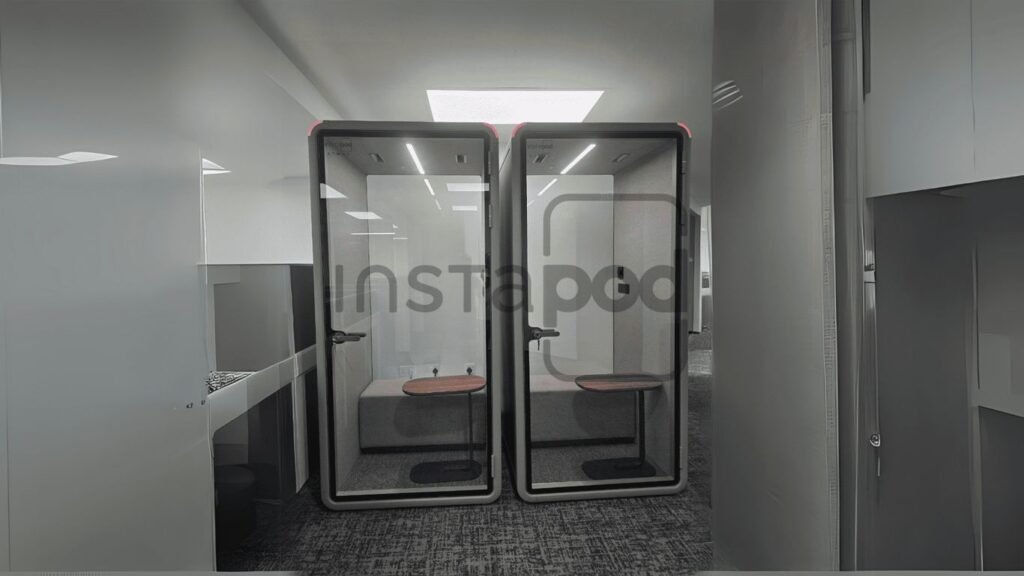 Two modern, glass-walled phone booths in a workspace.