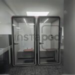 Two modern, glass-walled phone booths in a workspace.