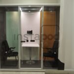 Modern soundproof booth with chairs and a table inside.