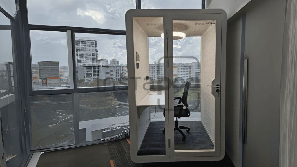 Modern office pod with glass walls and a desk inside.