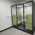 A modern glass pod with green seating for privacy and comfort.