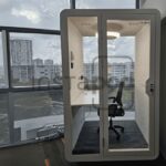Modern office pod with glass walls and a desk inside.