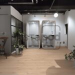 Modern office space with two glass phone booths and plants.