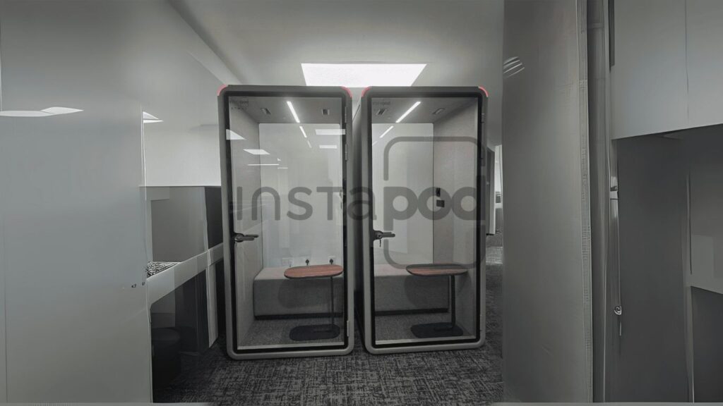 Two modern, glass-walled phone booths in a workspace.