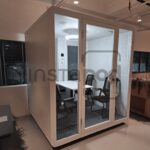A modern, glass-walled meeting pod in an office setting.