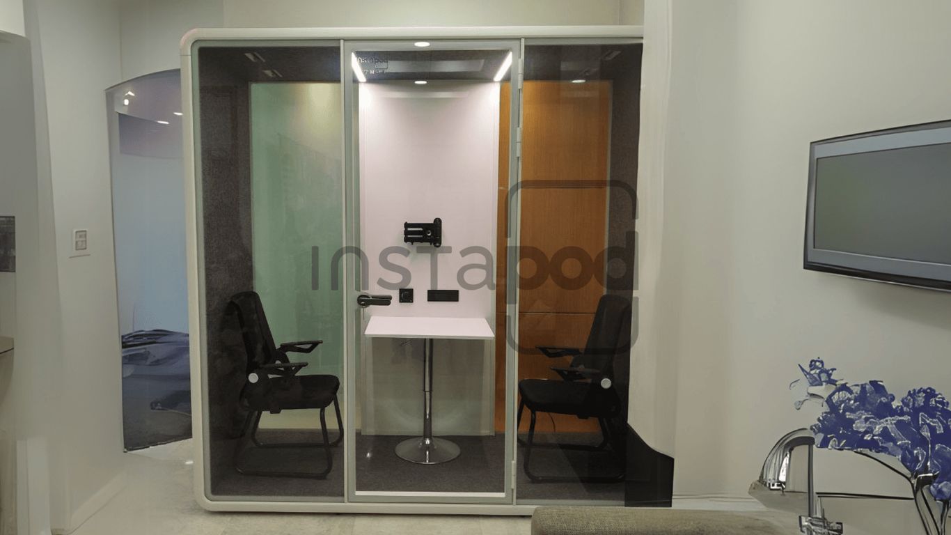 Modern soundproof booth with chairs and a table inside.