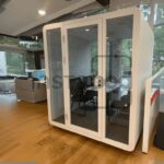 Modern office space featuring a glass meeting pod and seating.